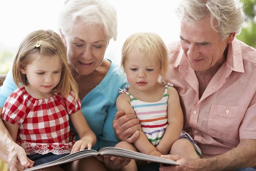 Grandparents And Grandchildren Reading Book On Garden Seat